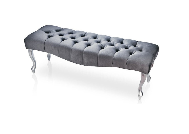 May include: A gray tufted bench with silver legs. The bench has a curved shape and a button tufted design.