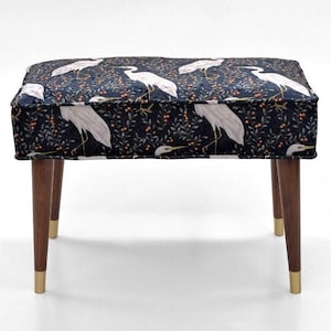 May include: A black and white patterned footstool with a dark blue background and white birds. The footstool has four wooden legs with gold tips.