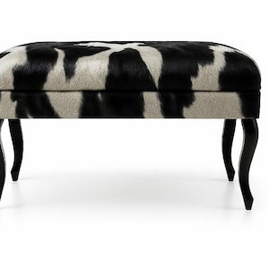 May include: An upholstered ottoman with a black and white cowhide pattern. The rectangular top rests on four curved black legs. This decorative furniture piece adds a touch of luxury to any living space.