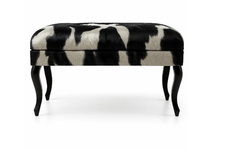 May include: An upholstered ottoman with a black and white cowhide pattern. The rectangular top rests on four curved black legs. This decorative furniture piece adds a touch of luxury to any living space.