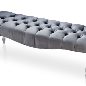 May include: A gray tufted bench with silver legs. The bench has a curved shape and a tufted design.