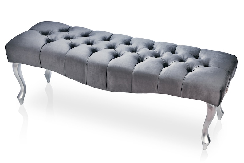 May include: A gray tufted bench with silver legs. The bench has a curved shape and a tufted design.