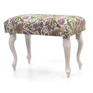 Pode incluir: Um banco estofado branco com quatro pernas brancas. O banco tem um tecido estampado paisley com cores verde, rosa e azul.
