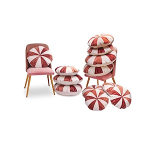 Op de afbeelding: Een set ronde kussens met roze en witte strepen. De kussens zijn gestapeld op een stoel en op de vloer.