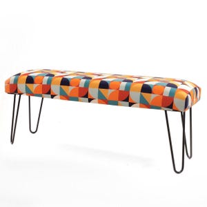 Pode incluir: Banqueta de estilo moderno de meados do século com um padrão geométrico em laranja, azul, amarelo e branco. A banqueta tem um assento retangular e pernas de grampo pretas. O assento tem aproximadamente 122 cm de comprimento.