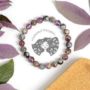 May include: A purple, grey, and black gemstone bracelet with a logo that says "Enchanted Therapist".
