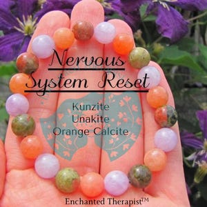 May include: A bracelet made with pink, green, and orange stones. The bracelet is labeled "Nervous System Reset" and lists the stones as Kunzite, Unakite, and Orange Calcite. The bracelet is held in a hand against a background of purple flowers.