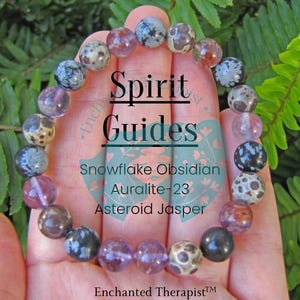 May include: A bracelet made with snowflake obsidian, Auralite-23, and asteroid jasper beads. The bracelet is on a hand and has the text "Spirit Guides" on it.