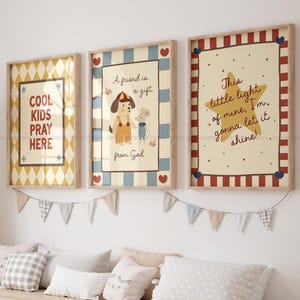Può includere: Tre stampe artistiche incorniciate con citazioni e illustrazioni ispiratrici. Una dice "COOL KIDS PRAY HERE" con un motivo a rombi. Un'altra dice "A friend is a gift from God" con un cane e un topo. La terza dice "This little light of mine, I'm gonna let it shine!"