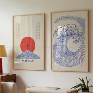 以下が含まれることがあります： ミニマルなデザインの額装されたプリント2枚。左側のプリントは、上に十字架のある赤い太陽、青い波、そして「He is Risen」というテキストが特徴です。右側のプリントは、青い波のデザインと「Be Still」というテキストが特徴です。