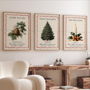 May include: Three framed art prints with a Christmas theme. The prints feature illustrations of a bell, a Christmas tree, and a candle. Each print has text in a decorative frame with a red border. The prints are displayed above a wooden table.