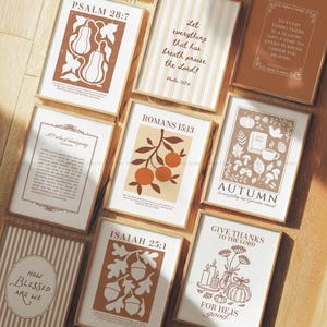 Könnte beinhalten: Eine Sammlung gerahmter Kunstdrucke mit botanischen und von der Schrift inspirierten Designs. Die Drucke zeigen Illustrationen von Kürbissen, Eicheln und Früchten sowie inspirierende Zitate und Bibelverse. Die Farbpalette umfasst Brauntöne, Beige und Weiß.