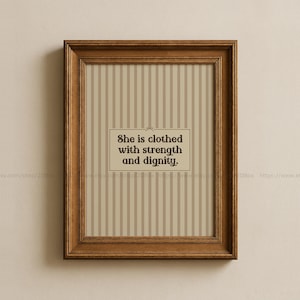 Può includere: Una stampa incorniciata con una cornice in legno marrone. La stampa presenta uno sfondo a righe beige e bianche con il testo "She is clothed with strength and dignity" in un riquadro rettangolare.