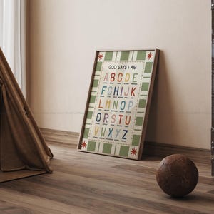 May include: A framed alphabet chart with the text "GOD SAYS I AM" and colorful letters. The chart has a green and white checkered background and is leaning against a wall. A brown soccer ball rests on the wooden floor.