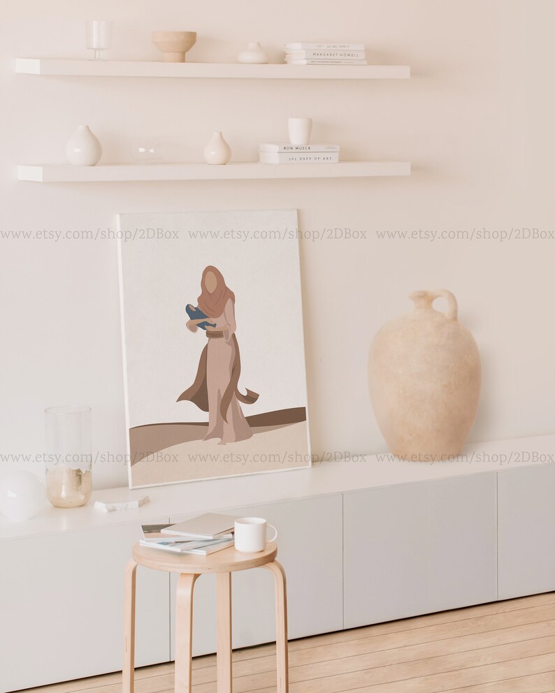May include: A digital art print featuring a woman in a brown dress holding a blue bird. The print is framed and hanging on a white wall above a white shelf with books and decorative objects.