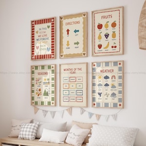 May include: A collection of framed educational posters with colorful designs. The posters display words like "Directions", "Fruits", "Seasons", "Months of the Year", and "Weather". The frames are beige with decorative borders, and the posters are hung on a white wall.