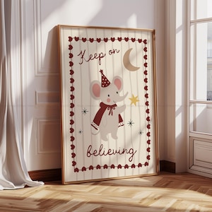 Könnte beinhalten: Ein gerahmter Druck mit einer Illustration eines Elefanten mit Partyhut und Umhang, der einen Stern hält. Der Druck trägt die Aufschrift "Keep on believing" und ist mit einem goldenen Rahmen und einem herzförmigen Design versehen.