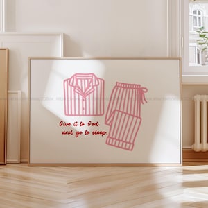 May include: A framed print with a cream background, showing a pink striped pajama set illustration. The image includes a pajama top and trousers. The text below reads, "Give it to God and go to sleep."