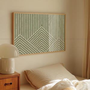 Könnte beinhalten: Gerahmter Wandkunstdruck mit einem geometrischen Design aus grünen und weißen Linien und Bergformen. Das Kunstwerk befindet sich in einem hellen Holzrahmen und hängt über einem Bett mit neutralfarbener Bettwäsche.