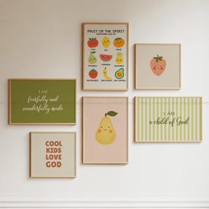 May include: A set of framed art prints with light wood frames. The prints display colourful fruit illustrations, including a pear, strawberry, and avocado, alongside inspirational text such as "Fruit of the Spirit" and "I am fearfully and wonderfully made."