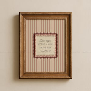 Könnte beinhalten: Ein gerahmter Druck mit einem braunen Holzrahmen. Der Druck zeigt einen gestreiften Hintergrund in Creme und Rosa. Ein quadratisches, dekoratives Element in der Mitte enthält den Text "Jesus loves me this I know for the Bible tells me so."