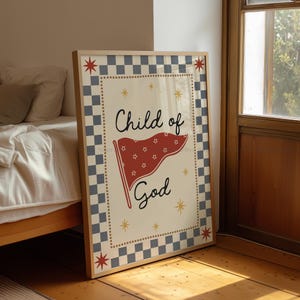 May include: A framed art print featuring the words "Child of God" with a red flag illustration. The artwork has a cream background with a checkered border in blue and gray. Decorative star accents and a wooden frame complete the design.