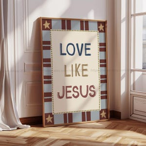 Könnte beinhalten: Ein gerahmter Druck mit den Worten "LOVE LIKE JESUS" in Marineblau, Beige und Burgunderrot. Der Druck hat einen beigefarbenen Hintergrund mit einem blau-rot gestreiften Rand, goldenen Sternen und einem goldenen Rahmen. Der Druck lehnt an einer weißen Wand.