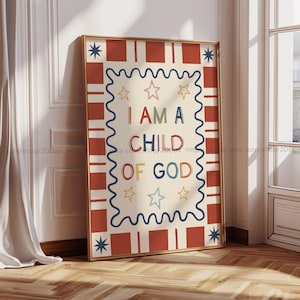May include: A framed art print with the text "I AM A CHILD OF GOD" in colorful letters. The artwork features a cream-colored background with a wavy blue border and star accents. The frame has a gold finish and is leaning against a wall.