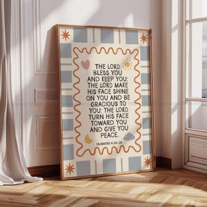 Könnte beinhalten: Ein gerahmter Druck mit beigem Rand und hellblau-weiß kariertem Hintergrund. Der Druck zeigt den Text "THE LORD BLESS YOU AND KEEP YOU" mit dekorativen Illustrationen von Sonne, Mond und Sternen. Der Text stammt aus Numeri 6:24-26.