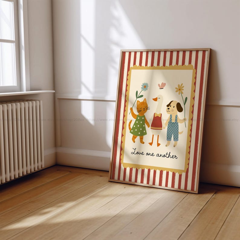 May include: A framed print featuring a cat, goose, and dog holding hands and flowers. The cat wears a green dress, the goose a red top, and the dog blue overalls. The print has a cream background with the words "Love one another". The frame has red and white stripes.