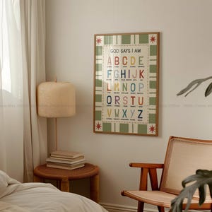 May include: A framed poster with the text "GOD SAYS I AM" and the alphabet in various colors. The poster has a green and white checkered pattern and is surrounded by a wooden frame. The poster is hanging on a white wall.