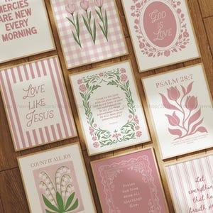 May include: A selection of framed art prints in light pink and white. The prints display floral patterns, inspirational quotes, and text including "God is Love" and "Love Like Jesus". The frames have a natural wood finish.