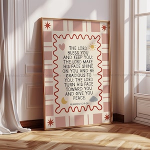 Könnte beinhalten: Ein gerahmter Druck mit goldenem Rahmen, der den Text "THE LORD BLESS YOU AND KEEP YOU" und andere inspirierende Worte zeigt. Der Hintergrund hat ein rosa-cremefarbenes Karomuster mit dekorativen Sternen, Herzen, Sonnen, Monden und Wolken. Der Text stammt aus Numeri 6:24-26.