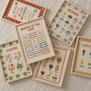 May include: A collection of framed educational posters. The posters feature various themes, including months of the year, weather, seasons, fruits, and directions. Each poster has a light wood frame and colorful illustrations and text.
