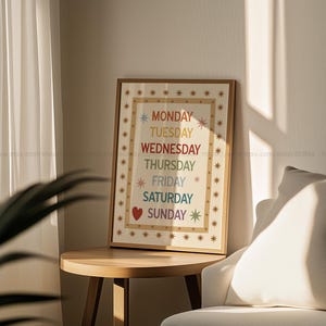 May include: A framed print on a wooden table displays the days of the week in a rainbow color scheme. The days are listed vertically, with a heart symbol next to Saturday. The frame is surrounded by star-shaped designs.