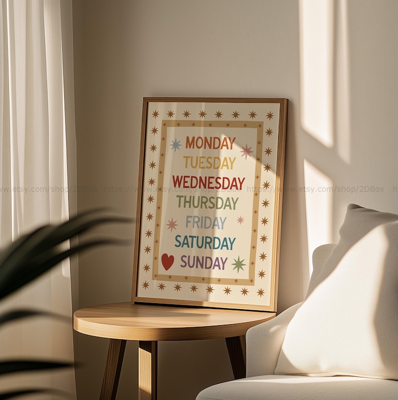May include: A framed print on a wooden table displays the days of the week in a rainbow color scheme. The days are listed vertically, with a heart symbol next to Saturday. The frame is surrounded by star-shaped designs.