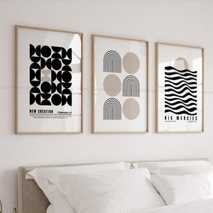 May include: Three framed art prints with minimalist designs. The prints feature geometric shapes in black and beige on a white background. Text includes "NEW CREATION" and "HIS MERCIES". The frames are a light wood color.