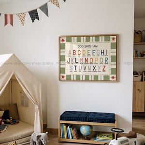 Può includere: Un grafico dell'alfabeto incorniciato con il testo "GOD SAYS I AM" e lettere colorate. Il grafico è esposto nella stanza di un bambino, insieme a una piccola tenda, una panca con libri e un'auto giocattolo. Una ghirlanda di bandierine è appesa sopra.