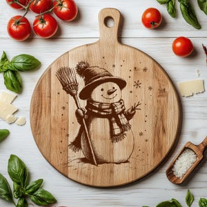 May include: A round wooden cutting board with a handle, featuring a detailed illustration of a snowman wearing a hat and scarf, holding a broom. Snowflakes are scattered around the snowman. The board is surrounded by tomatoes, basil, and cheese.