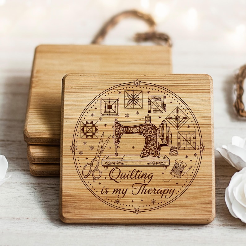 May include: Square wooden coasters with a laser-etched design. The design includes a vintage sewing machine, scissors, and the text "Quilting is my Therapy" within a circular frame. The coasters are made of light-coloured wood.