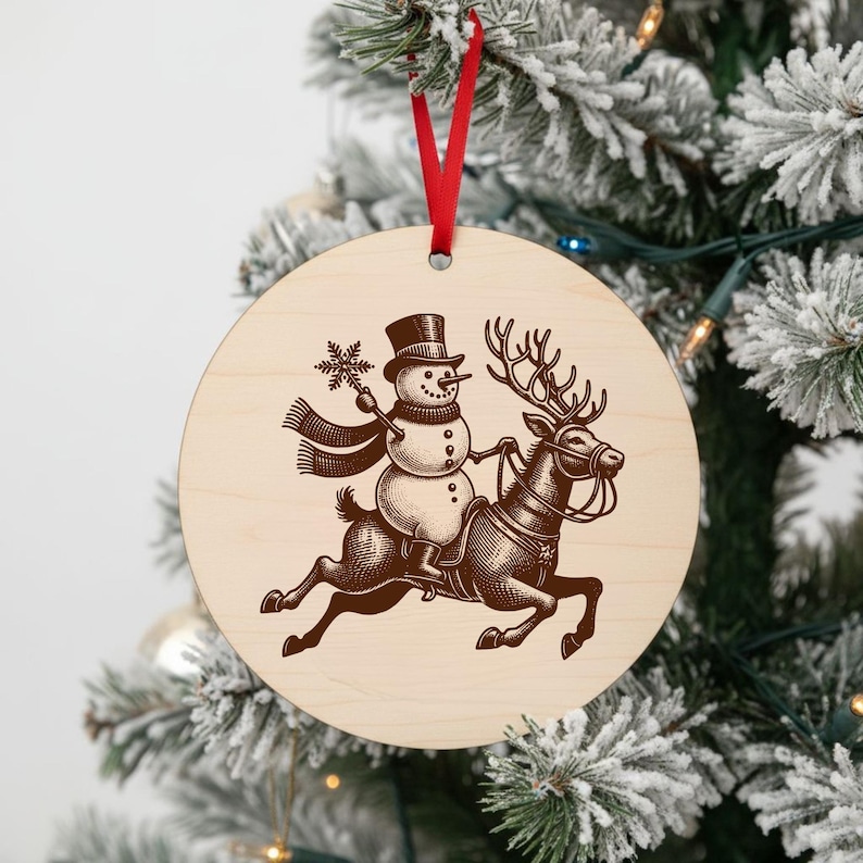May include: A round wooden Christmas ornament with a snowman riding a reindeer. The snowman wears a top hat and scarf, holding a snowflake. The reindeer has a harness. A red ribbon is attached for hanging.