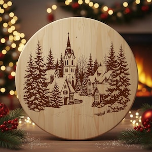 May include: A round wooden cutting board with a detailed etched winter village scene. The design features a church, houses, and evergreen trees. The board is light-colored wood, perfect for holiday decor or kitchen use.
