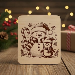 May include: A wooden Christmas-themed plaque featuring a snowman and a penguin, both wearing hats and scarves. The snowman holds a candy cane. Snowflakes are scattered around the figures. The design is in shades of brown and beige.