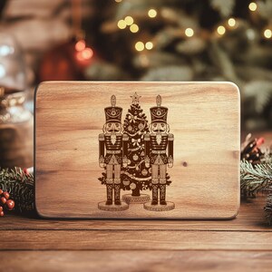 A wooden board with a decorative image of two nutcracker men standing next to a Christmas tree.