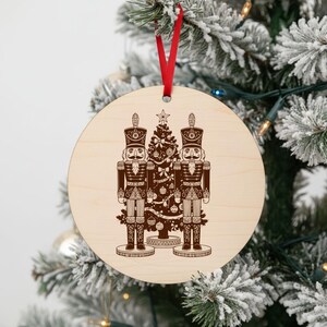 A wooden ornament with a nutcracker and Christmas tree design hangs on a decorated Christmas tree.