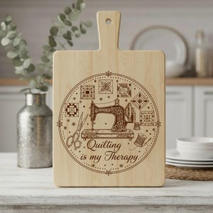 May include: Wooden chopping board with a handle, featuring a decorative design. The design includes a vintage sewing machine, scissors, and the text "Quilting is my Therapy." Various quilt block patterns surround the sewing machine. The board is made of light-coloured wood.