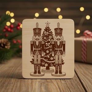 Pode incluir: Base quadrada de madeira com um design gravado em castanho com dois quebra-nozes ladeando uma árvore de Natal. Os quebra-nozes usam chapéus altos e seguram pequenas xícaras. A árvore é decorada com enfeites e uma estrela.