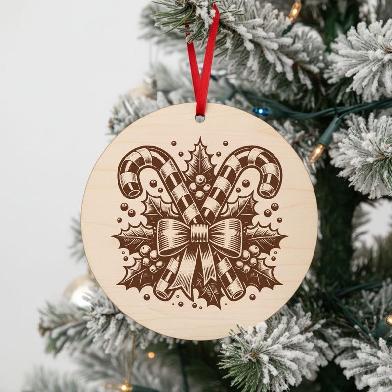 May include: Round wooden Christmas ornament with a red ribbon. The ornament features a brown engraved design of two candy canes, holly leaves, berries, and a bow. The ornament is hanging on a snowy Christmas tree.