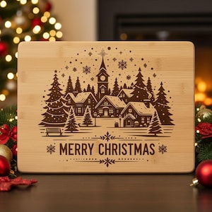 May include: A rectangular bamboo cutting board with a laser-etched Christmas village scene. The design features a church, houses, trees, and the words "MERRY CHRISTMAS". The board is light brown with a natural wood grain.
