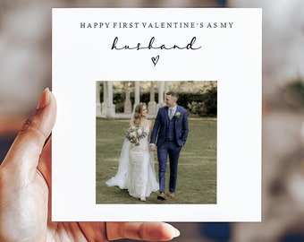 Puede incluir: Una tarjeta blanca con el texto "Happy First Valentine's as my husband" y un pequeño símbolo de corazón. Una foto de una novia y un novio caminando de la mano en un jardín está en el centro de la tarjeta.